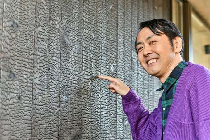 焼杉張りの外壁を指差す田中さん