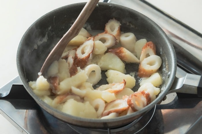 水気がなくなってきたら火を強め、全体をヘラで混ぜながら水気を飛ばし、煮崩れたジャガイモをちくわに絡ませる。火を止めて器に盛り、小ネギをトッピングして完成。