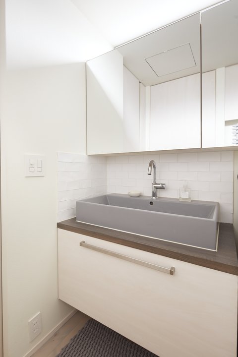 大きな鏡とグレーの洗面ボウルが印象的な洗面室