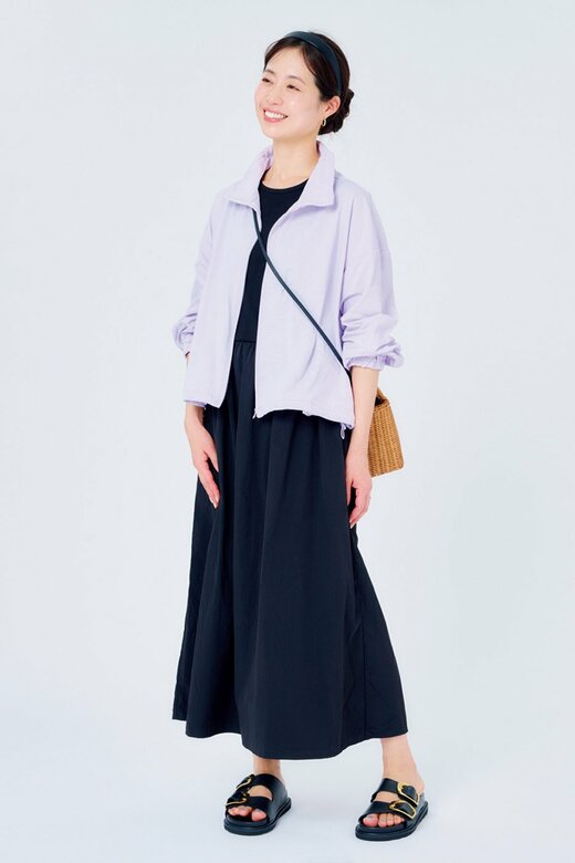 ワンピースに上着を羽織って笑顔で立つ女性