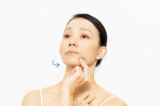 フェイスラインを指でつまみ、首を左右に振る女性