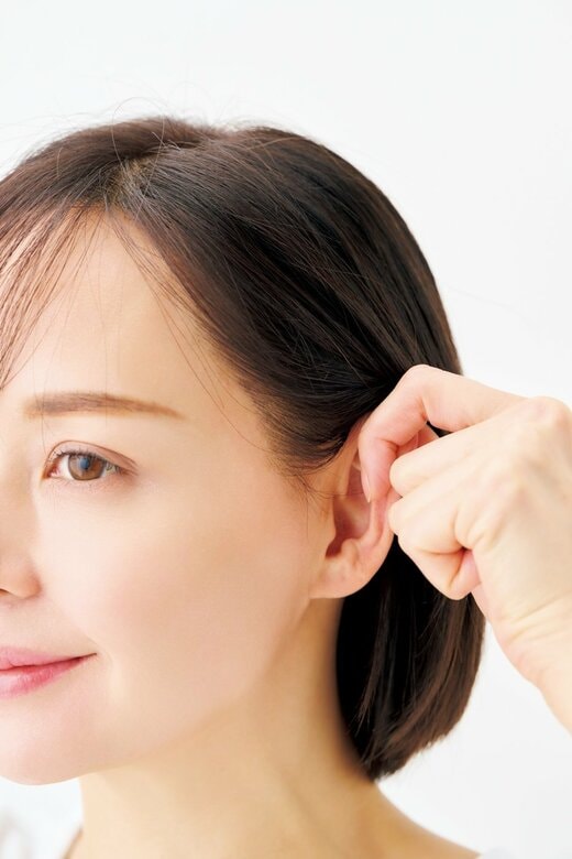 親指と人さし指の指先で耳の上部をはさむ女性