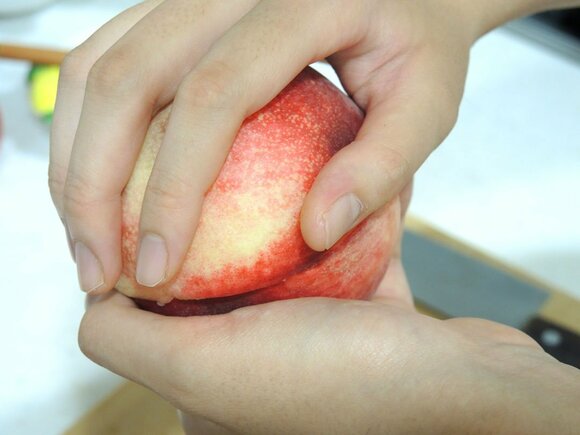 手で白桃をねじって2つに分け、種をくり抜く