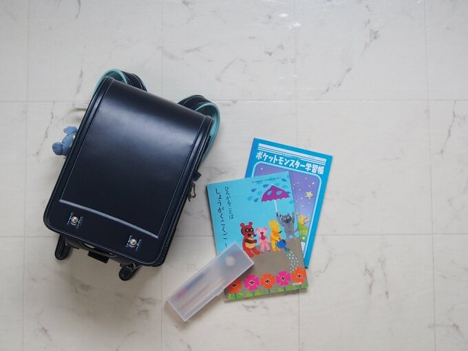 床に置かれた黒いランドセルとノート2冊、筆箱