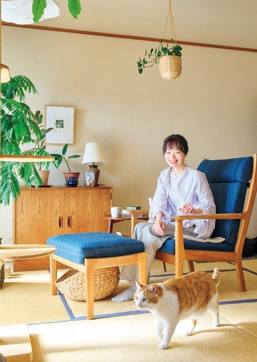 自宅の椅子に座ってくつろぐ女性とそばを歩く猫