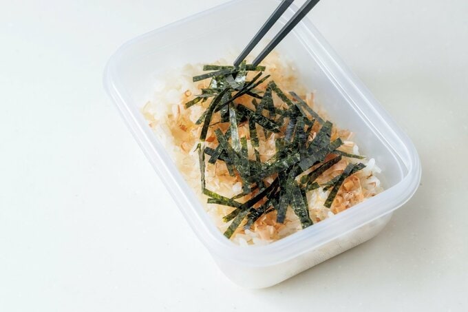 容器に入ったご飯の上にカツオ節と焼きのりをのせる