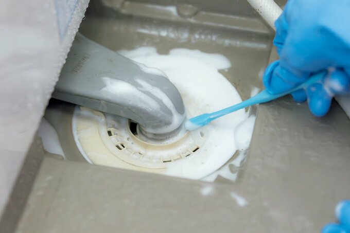 歯ブラシで排水口のにおい取りをする手元