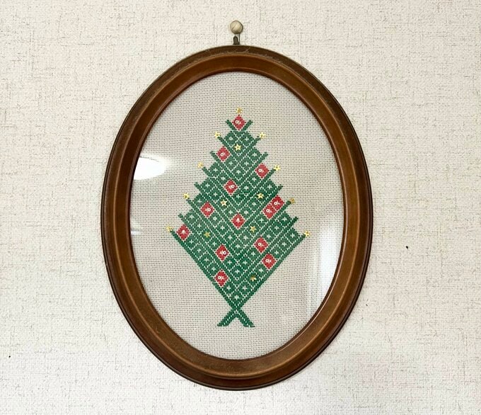 木製の額に入って壁に飾られた緑と赤のクリスマスツリーの刺し子作品
