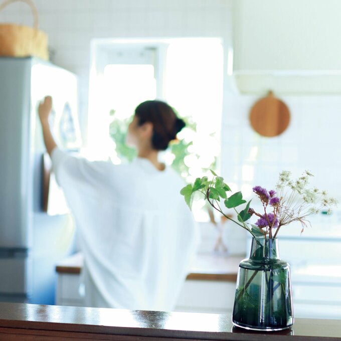 白が基調のキッチンで、冷蔵庫に何かを貼る女性