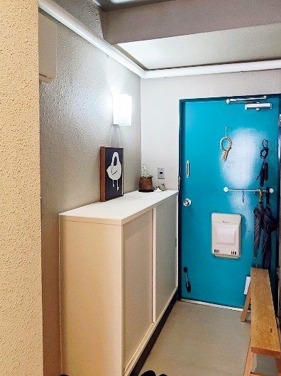 白い小さな靴箱と水色のドアが目をひく玄関