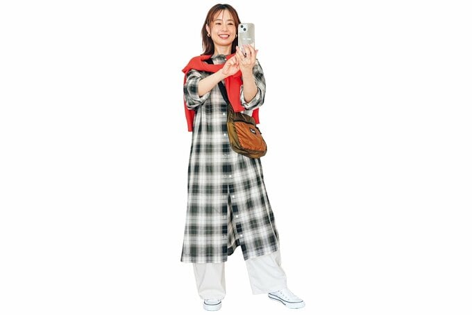 スマホで写真を撮っている、オレンジニットを肩がけした女性