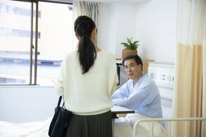 病院のベッドにいる男性と立っている女性
