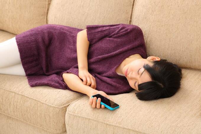 ソファでスマホをもって眠る女性