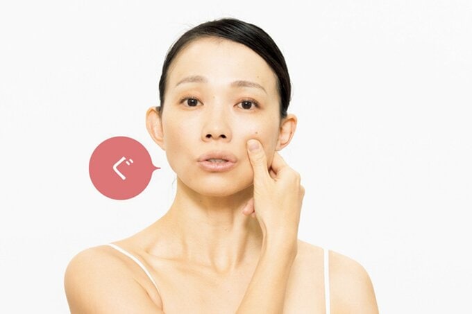 頬骨をつまみ「ぐ」の口の動きをする女性