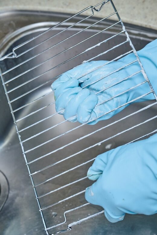 青いゴム手袋をはめた両手で魚焼きグリルの網を磨いている手元