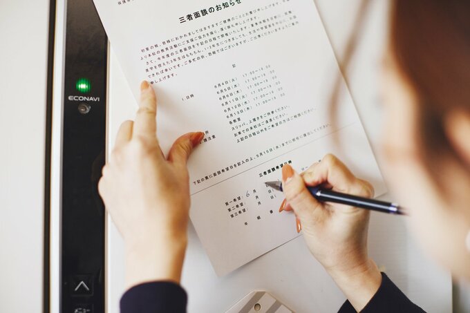 冷蔵庫の扉の上で提出物を記入する女性