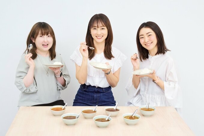 ご飯が盛られた皿とスプーンを持つ女性3名と数種類のレトルトカレー