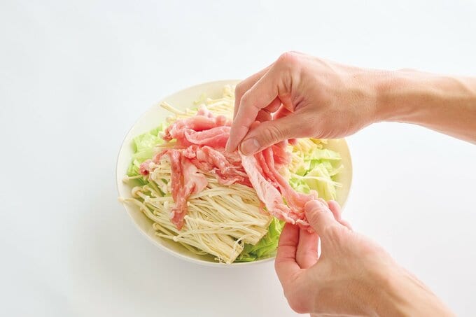 耐熱皿に重ねられたキャベツ、エノキ、豚肉