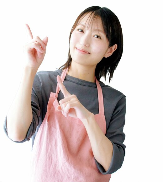 左上を両手で指さしてほほ笑む長谷川さん