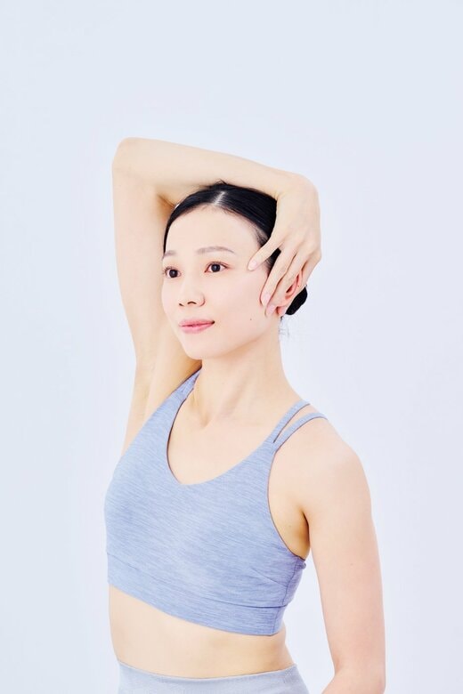 右手を頭の上から顔の左横に当てる女性