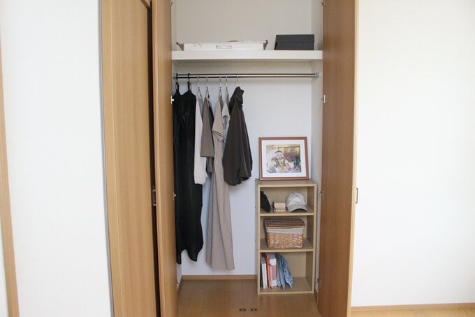 クローゼットに少しの衣服がかかっている。床にカラーボックスがありものが収納されている。