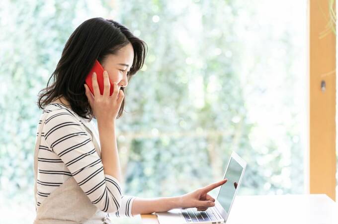 スマホを片手にパソコンを指さす女性