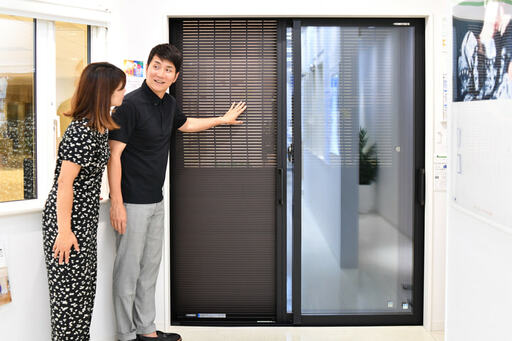 黒っぽい雨戸の前に立つ２人