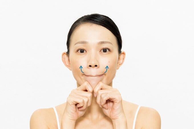 人さし指をあごに当て、口を閉じたまま口角を上げる女性