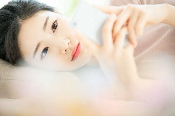 横になってスマホを見る女性