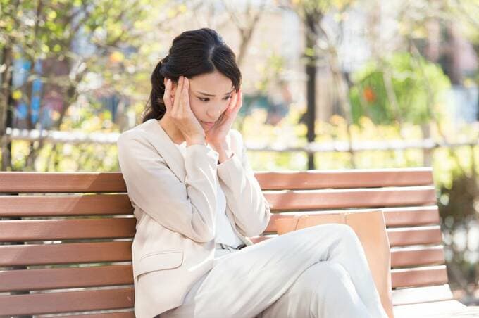 女性がベンチに座ってこめかみを押さえているイメージ