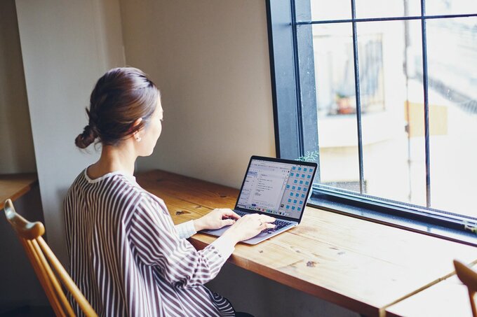 窓際で座ってパソコン作業をする女性