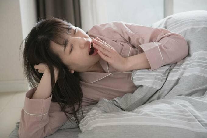 布団にあくびをするパジャマ女性