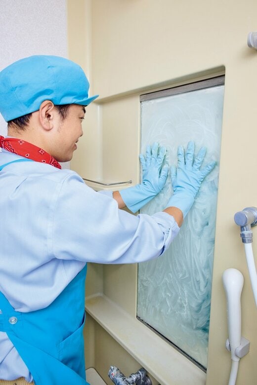 ゴム手袋をはめて、浴室の鏡を掃除している男性