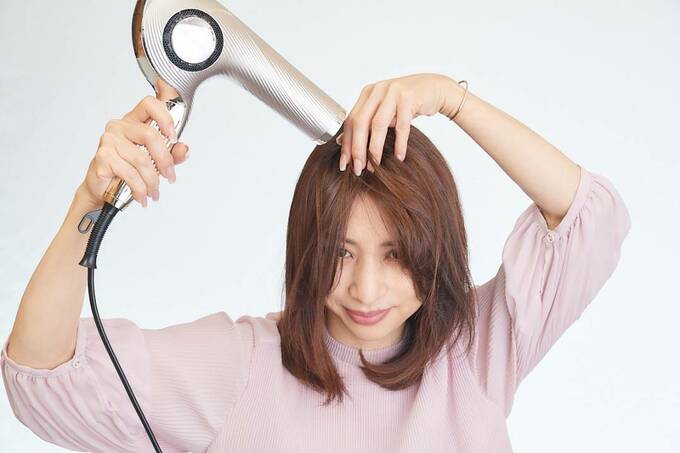 ドライヤーで分け目を乾かしている女性