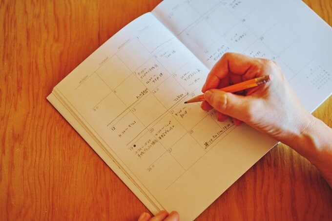 鉛筆でスケジュール帳に書き込んでいる手元
