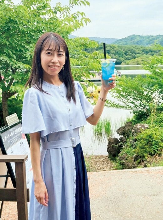 ドリンクを持って立つ、水色とネイビーのワンピースを着た女性