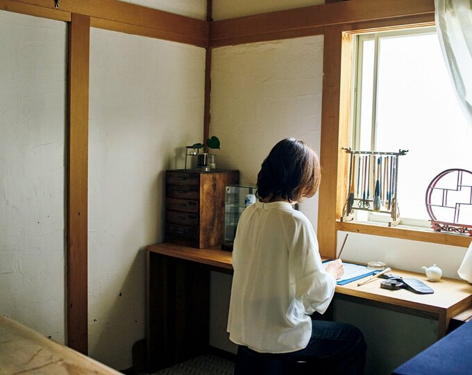 白のトップスを着た女性が書道をしている様子