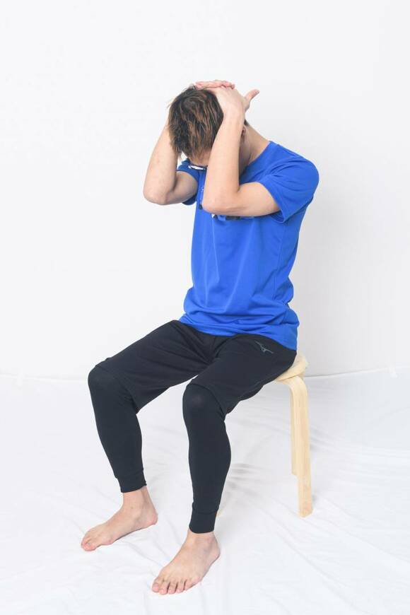 イスに座り頭の後ろで両手を組む