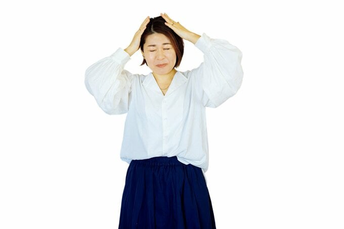 白い服の女性が頭を抱える様子