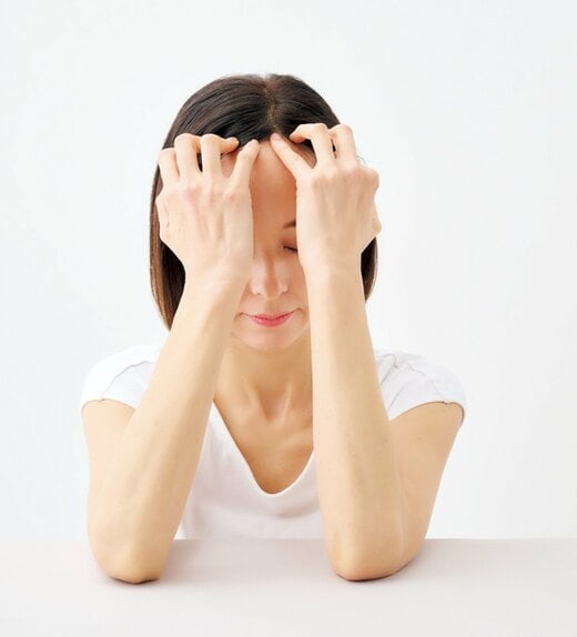 指で髪の生え際を押し上げる女性