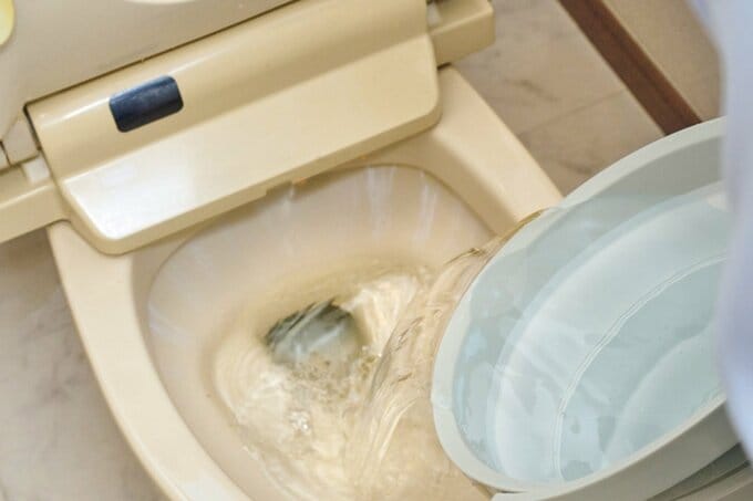 バケツの水を便器に流し入れている様子
