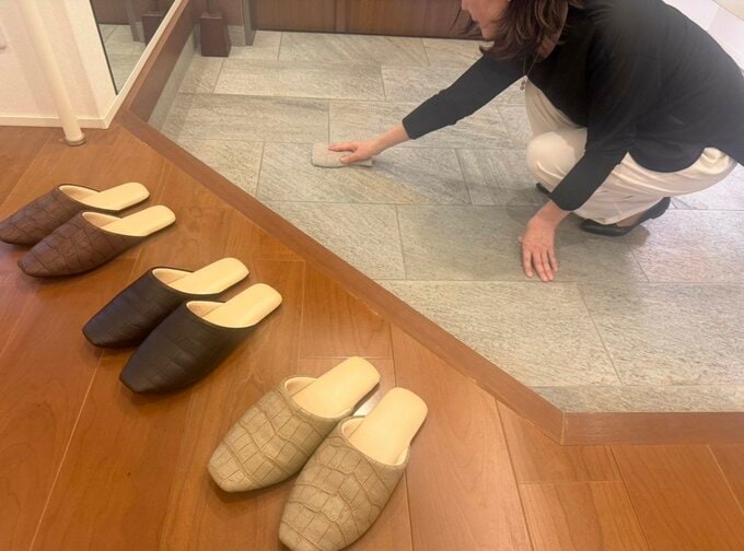 玄関の土間でしゃがんで、スポンジで掃除している。床に室内スリッパが3足並んでいる。