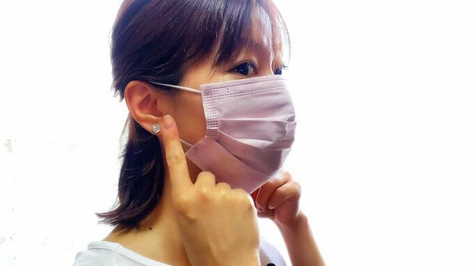 耳をおさえるマスクをつけた女性