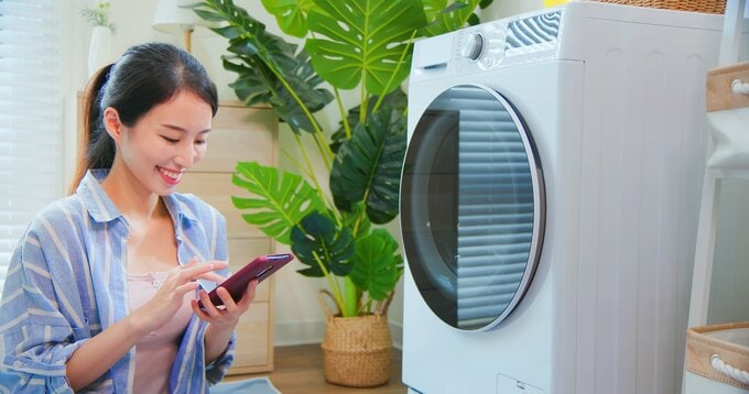 洗濯機の前でスマホを触る女性