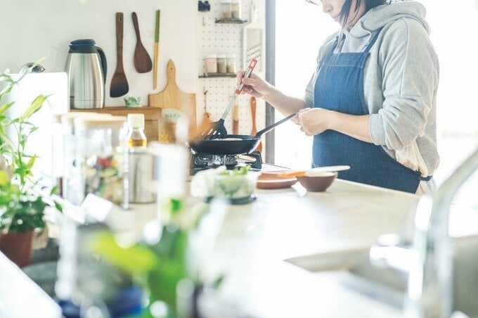 有孔ボードに調理器具がつり下げられているキッチンで料理をする女性