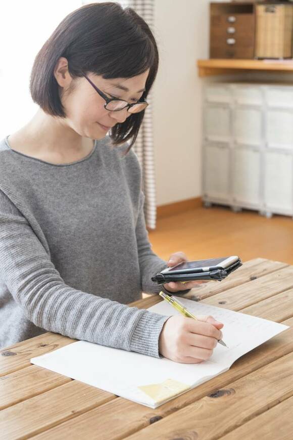 スマホを持ちながら書く女性