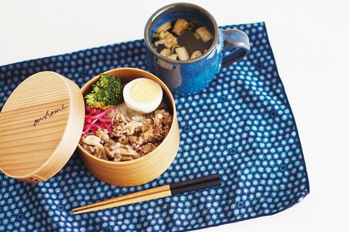 ふたが開いたお弁当とマグカップに入ったお味噌汁