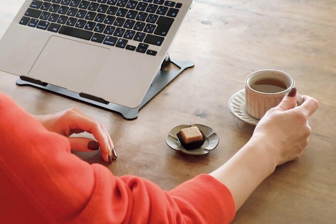 ノートパソコンに向かい、コーヒーカップに手を伸ばす女性