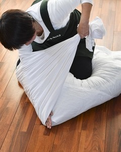 布団をひざで押さえ、シーツの間に手を差し込んで、しっかりと折り目をつけながら左右のシーツを引っぱります。