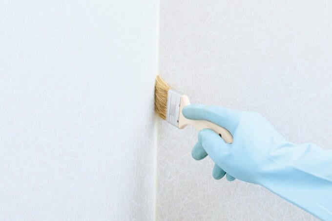 水色のゴム手袋をつけてハケを壁の角にあてている